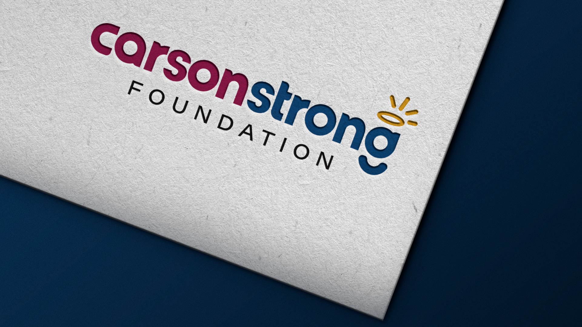 Logo of Carson Strong Foundation, featuring stylized text with "carson" in maroon, "strong" in blue, and "foundation" in black. A small yellow halo is above the second letter 'o'.