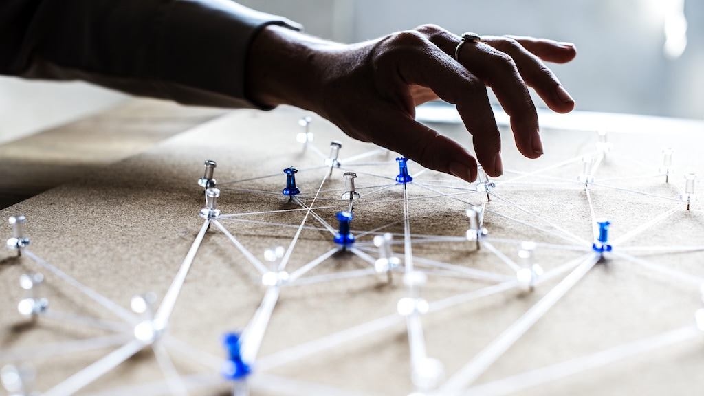 A hand hovers over a board with interconnected pushpins and strings, illustrating a network or strategic planning concept.