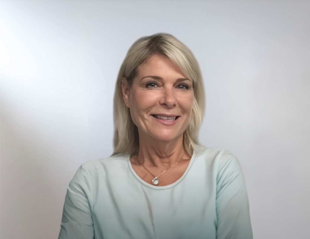 A woman with blonde hair and a light blue top smiles at the camera against a plain, light-colored background.
