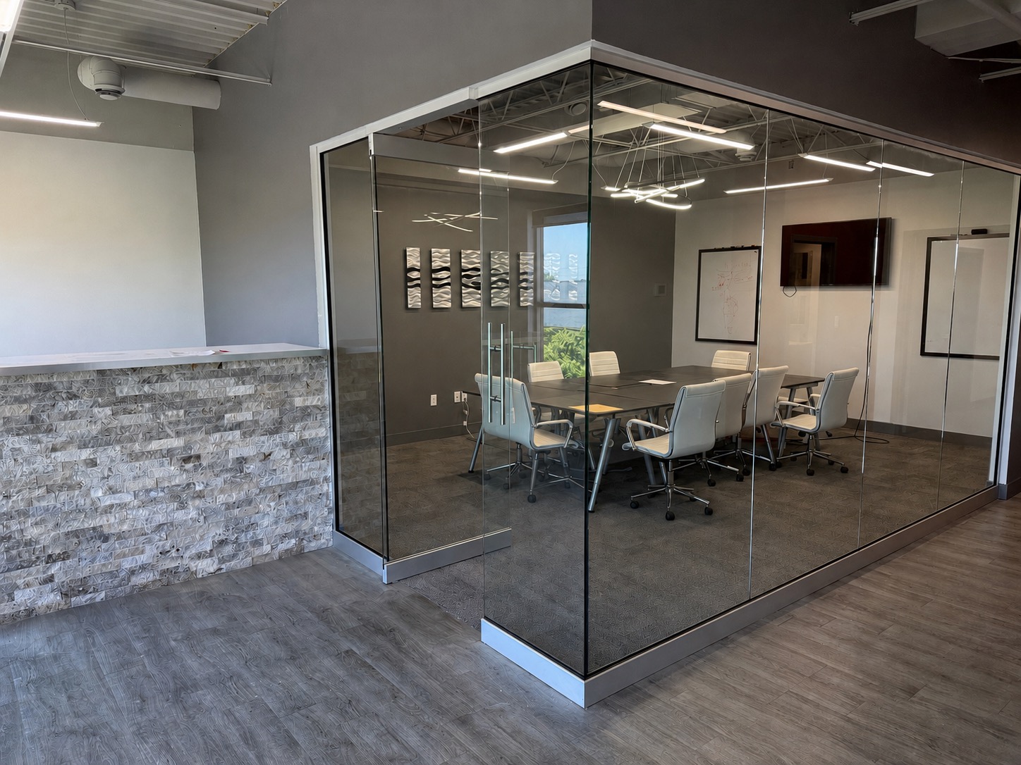 Modern office with a stone reception counter and a glass-walled conference room containing a table, white chairs, and wall-mounted displays—perfectly suited for the dynamic pace of DMG moving and collaborative business meetings.
